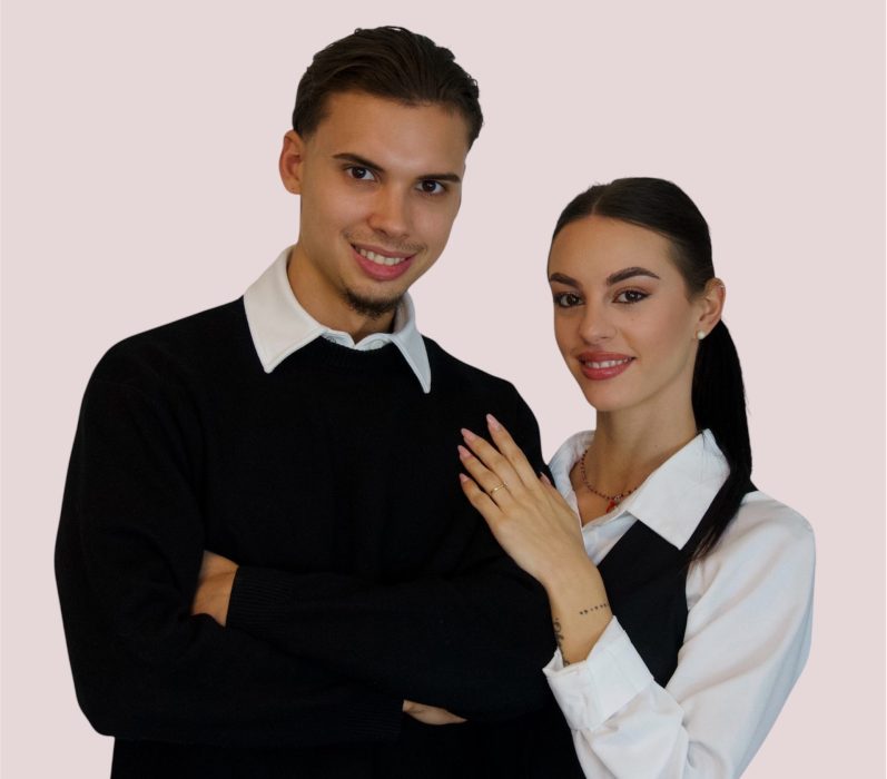 Junges Paar posiert freundlich, der Mann in schwarzem Pullover und die Frau in eleganter Bluse.